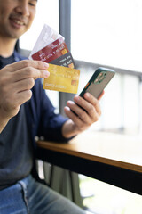 A man is holding a credit card and a cell phone. He is sitting at a table. Concept of modern life and the importance of technology in our daily lives
