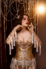 Young Caucasian woman in ornate cabaret outfit with golden corset, standing on dark stage under chandelier, front view. Concept: cabaret, glamour, theatrical show, vintage performance.