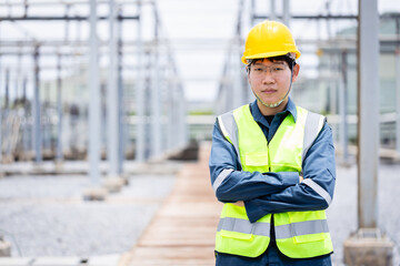 Engineer is working at high voltage power substation wearing safety gear while performing inspection and check of electrical infrastructure to ensure proper operation