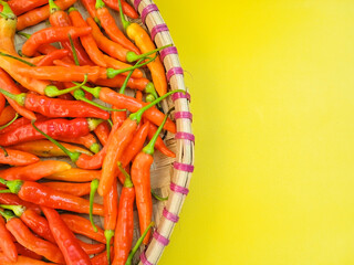 Fresh red and orange chili peppers in traditional bamboo tray isolated on yellow background. Close...