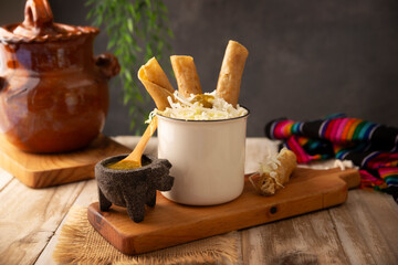 Flautas Ahogadas (Drowned Flautas) Golden tacos made with fried corn tortillas, filled with chicken or beef, and served in a glass or cup containing salsa or broth, lettuce, sour cream, and cheese.