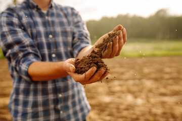 Hands of a young farmer holding fertile soil in his hands against the backdrop of an agricultural...