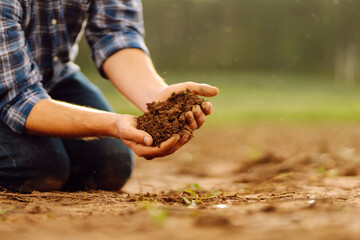 Hands of a young farmer holding fertile soil in his hands against the backdrop of an agricultural...