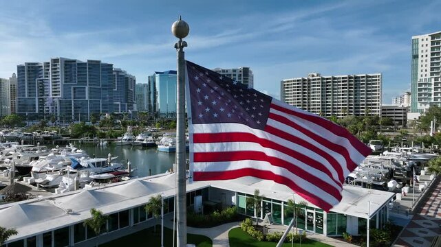 Flying flag of United States America on flagpole In front of marina port in Sarasota.Aerial close orbit shot. Residential and towers of downtown in background.