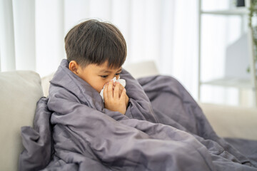 Young asian boy sneezing or blowing his nose and mouth with tissue, cold allergies or illness, health, virus and flu season, RSV, Influenza, childcare and hygiene practices, especially for children