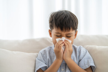 Young asian boy sneezing or blowing his nose and mouth with tissue, cold allergies or illness,...