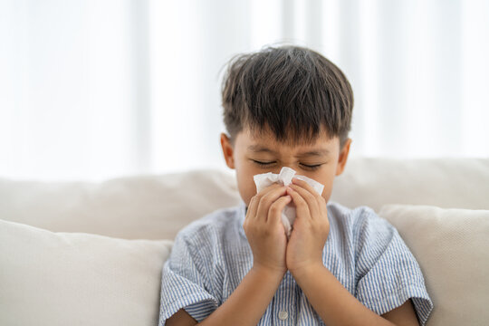 Young asian boy sneezing or blowing his nose and mouth with tissue, cold allergies or illness, health, virus and flu season, RSV, Influenza, childcare and hygiene practices, especially for children - Powered by Adobe