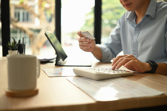 Close-up of hands managing digital finances with a credit card and calculator in a office