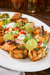 Grilled fish assortment with lime and herbs, rustic lighting, overhead composition
