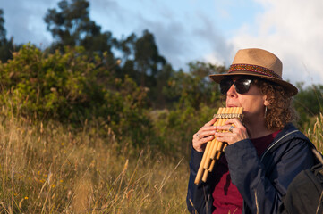 Woman playing andean pan flute in nature enjoying golden hour light © Martin Stock Studio