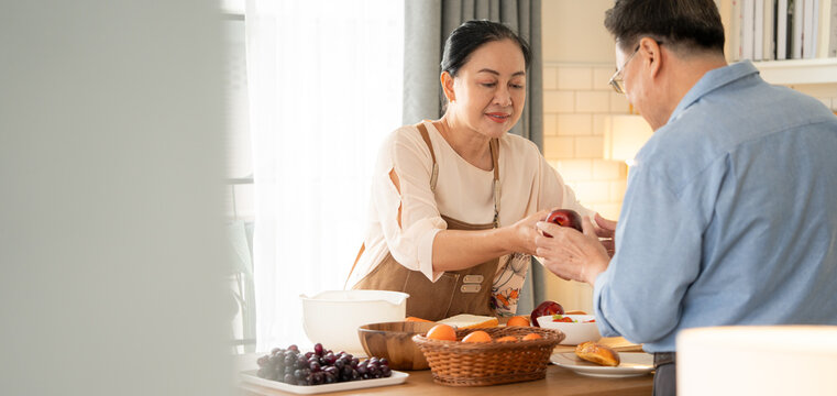 Asian senior couple cooking breakfast in the kitchen. husband helping wife on the morning weekend. Retired people enjoying lifestyle at the preparing counter