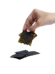A hand picking up a square piece of dried seaweed snack with a stack of seaweed sheets on a white background, isolated for commercial food presentation or packaging use.