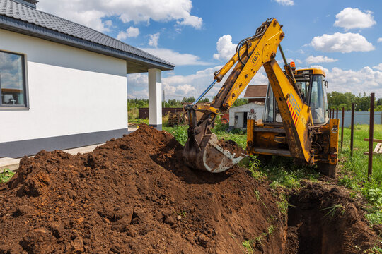 Russia. Samara, July 31, 2024: A wheeled excavator digs a trench to supply water to a private home on a summer day.