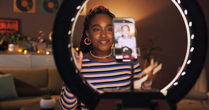 Black woman, influencer and phone with ring light at house for introduction, late live streaming or social media. Night, content creator and wave to audience, filming video or vlog tutorial with tips