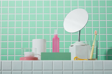 Bathroom counter with pastel skincare bottles and mirror against green mosaic tiles. Clean and styled washroom scene.