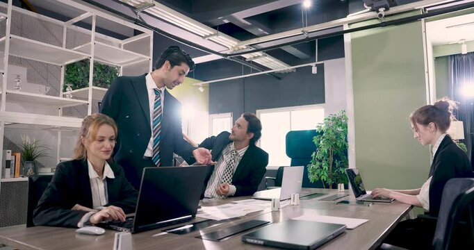 Office teamwork with diverse adult employees discussing task together manager guiding colleague while female assistant using laptop during active business meeting in modern professional environment