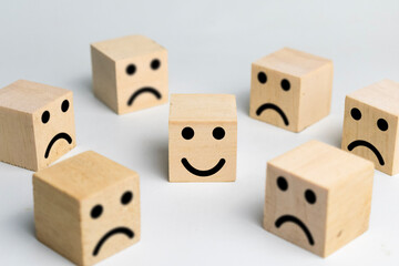 happy face in the center among sad face expression emoji on wooden blocks isolated on white background