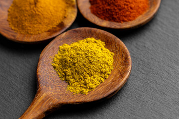 Colorful Spices on Wooden Spoons – Curry, Turmeric, and Paprika on Dark Slate Background
