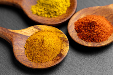 Colorful Spices on Wooden Spoons – Curry, Turmeric, and Paprika on Dark Slate Background