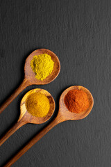 Colorful Spices on Wooden Spoons – Curry, Turmeric, and Paprika on Dark Slate Background