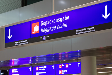 A blue information board in an airport terminal with arrows indicating downstairs to the baggage...