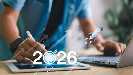 Businessman hand on laptop with digital 2026 goal, rocket launch and upward arrows. Futuristic...