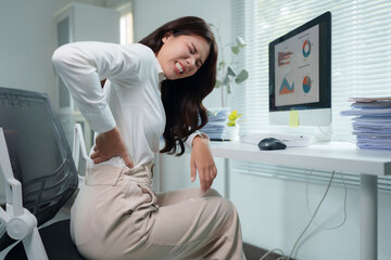 Young businesswoman suffering from back pain while working on computer at office
