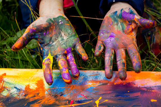 Child showing painted hands over colorful artwork