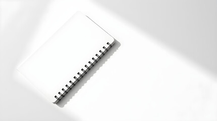 Blank spiral notepad on white table with window light creating shadows