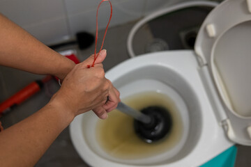 A woman's hand is using an air pump to solve a clogged toilet.