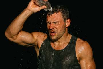 Athletic man pouring water over himself while exercising in dark setting