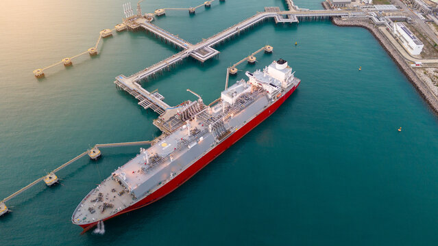 Aerial view of an LNG tanker docked at an offshore terminal with multiple pipelines, storage tanks, and an industrial complex. Captures global energy logistics