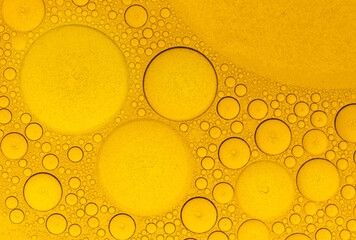 Macro abstract image of golden oil bubbles suspended in liquid, forming overlapping circular...
