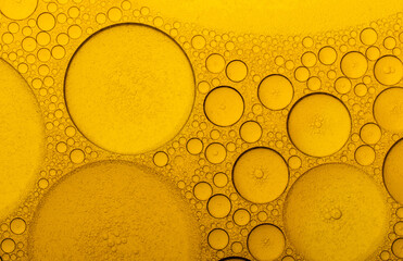 Macro abstract image of golden oil bubbles suspended in liquid, forming overlapping circular...