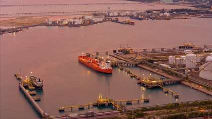 large oil tanker docked at a refinery terminal with multiple white storage tanks, complex pipeline...
