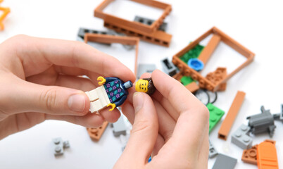 Naklejka premium Lego bricks on the table, child is building a minifigure. Editorial illustrative image of popular plastic blocks.