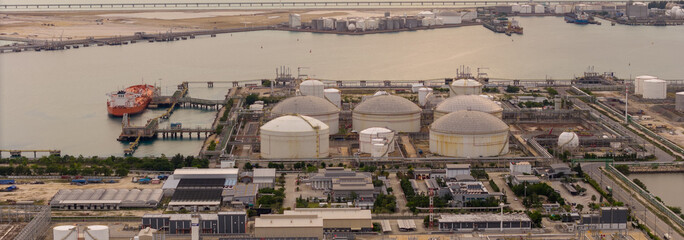 large industrial oil and gas storage tanks at a coastal refinery terminal during dusk. Tanker ships...