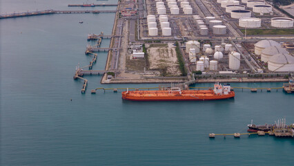 large oil tanker docked at a refinery terminal with multiple white storage tanks, complex pipeline networks, and offshore loading platforms. Represents global oil logistics