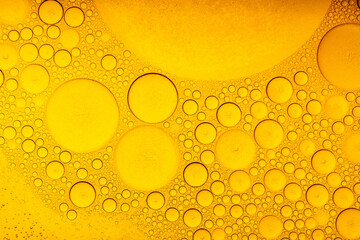 Macro abstract image of golden oil bubbles suspended in liquid, forming overlapping circular...