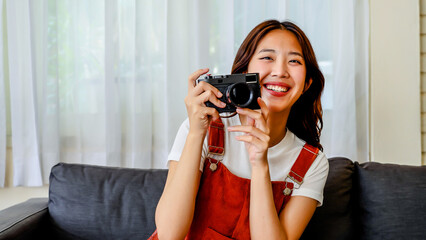 Beautiful Young Female Photographer happily taking pictures playing with friends in the living room, making shots, looking into the camera's video lens and smiling.