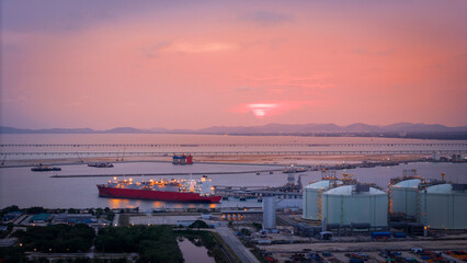 Aerial view of an LNG tanker docked at an offshore terminal with multiple pipelines, storage tanks, and an industrial complex. Captures global energy logistics