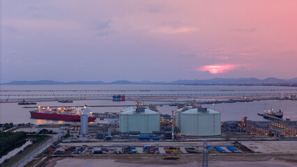 Aerial view of an LNG tanker docked at an offshore terminal with multiple pipelines, storage tanks, and an industrial complex. Captures global energy logistics