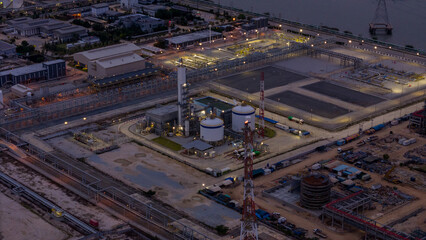 large industrial oil and gas storage tanks at a coastal refinery terminal during dusk. Tanker ships docked at long piers highlight the global energy transport infrastructure.