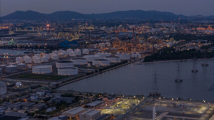 large industrial oil and gas storage tanks at a coastal refinery terminal during dusk. Tanker ships docked at long piers highlight the global energy transport infrastructure.