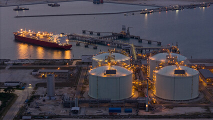 Aerial view of an LNG tanker docked at an offshore terminal with multiple pipelines, storage tanks, and an industrial complex. Captures global energy logistics