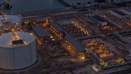 LNG storage tanks and terminal facility at dusk, showcasing large cylindrical containers, offshore piers, and cargo ships. Industrial landscape representing global liquefied natural gas
