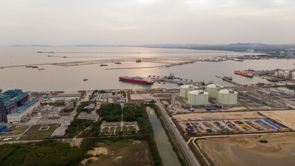 Aerial view of an LNG tanker docked at an offshore terminal with multiple pipelines, storage tanks, and an industrial complex. Captures global energy logistics