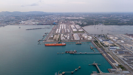 large oil tanker docked at a refinery terminal with multiple white storage tanks, complex pipeline networks, and offshore loading platforms. Represents global oil logistics