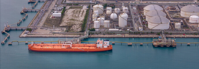 large oil tanker docked at a refinery terminal with multiple white storage tanks, complex pipeline networks, and offshore loading platforms. Represents global oil logistics