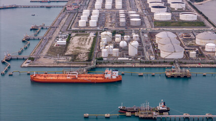 large oil tanker docked at a refinery terminal with multiple white storage tanks, complex pipeline networks, and offshore loading platforms. Represents global oil logistics